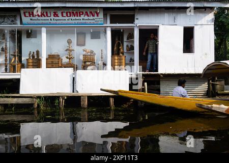 Lo shikara galleggia oltre una piccola azienda lungo il lago a Srinagar Foto Stock