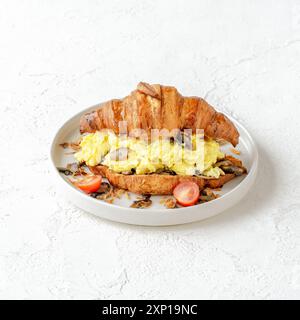 Croissant croccanti ripieni di uova strapazzate e funghi, guarniti con pomodori ciliegini e scalogni fritti Foto Stock