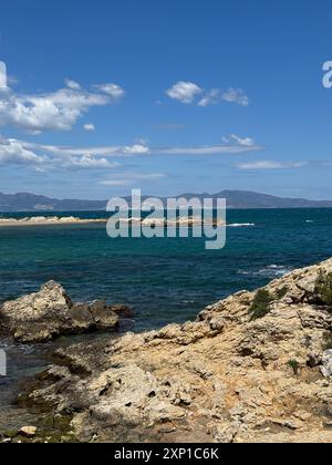 Una costa rocciosa con un oceano blu sullo sfondo. Le rocce sono sparse lungo il litorale e l'acqua è calma. La scena è tranquilla e s Foto Stock