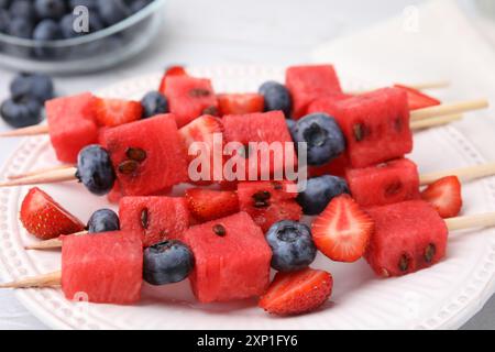 Spiedini con gustosi anguria, fragole e mirtilli su piatto bianco, primo piano Foto Stock