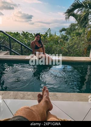 Una donna è seduta in piscina con le gambe in acqua Foto Stock