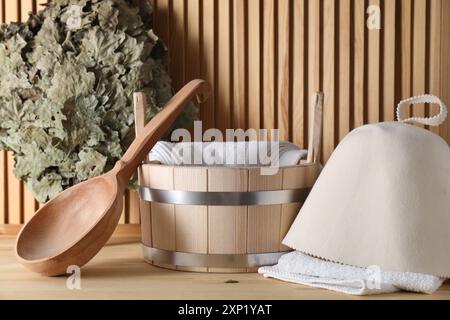 Frusta per sauna in quercia, cappello in lana di feltro, asciugamani, secchio e mestolo su una superficie in legno Foto Stock