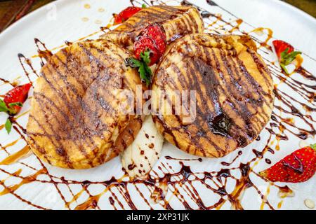 Pancake appena cucinati con banana, fragole e un filo di salsa al cioccolato su un piatto bianco in un ristorante per colazione. Foto Stock