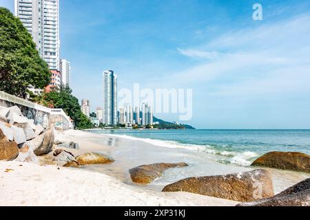 Una vista lungo la spiaggia di Tanjing Tokong a Penang, Malesia, con grattacieli alti e moderni, parte di un grattacielo cittadino sullo sfondo. Foto Stock