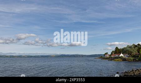 Cottage del piccolo villaggio di Balmerino punteggiati lungo la costa boscosa del Firth of Tay con la città di Dundee sullo sfondo. Foto Stock