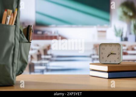Cose scolastiche e zaino sulla panchina della scuola in classe. Sfondo sfocato della lavagna sulla parete e sulla finestra con luce solare in entrata. Foto Stock