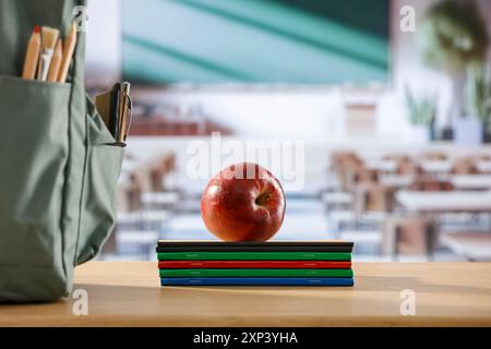 Cose scolastiche e zaino sulla panchina della scuola in classe. Sfondo sfocato della lavagna sulla parete e sulla finestra con luce solare in entrata. Foto Stock