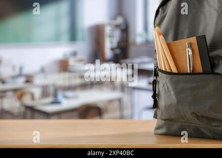 Cose scolastiche e zaino sulla panchina della scuola in classe. Sfondo sfocato della lavagna sulla parete e sulla finestra con luce solare in entrata. Foto Stock