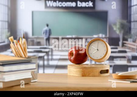 Cose scolastiche e zaino sulla panchina della scuola in classe. Sfondo sfocato della lavagna sulla parete e sulla finestra con luce solare in entrata. Foto Stock