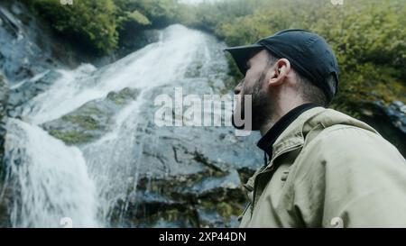 Il giovane turista va alla cascata di montagna tra grandi pietre. Escursionista che fa trekking, godendosi la cascata. Foto Stock