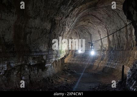 Interno illuminato di un tunnel buio con pareti aspre e formazioni rocciose Foto Stock