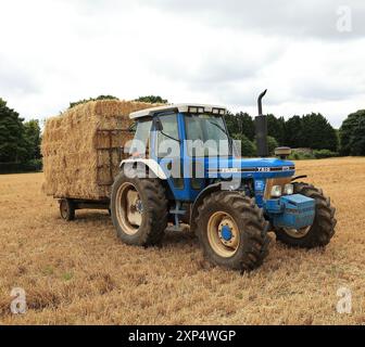 Stroud, Regno Unito, 6 agosto 2024. È ora di raccolta estiva per gli agricoltori del Gloucestershire, che utilizzano i loro trattori e rimorchi per radunarsi nelle balle. Foto Stock