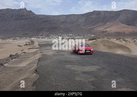 La strada che va dai bungalow Los Noruegos alla Caleta de Famara, con una Audi cabriolet rossa solitaria. Famara, Lanzarote. Foto Stock