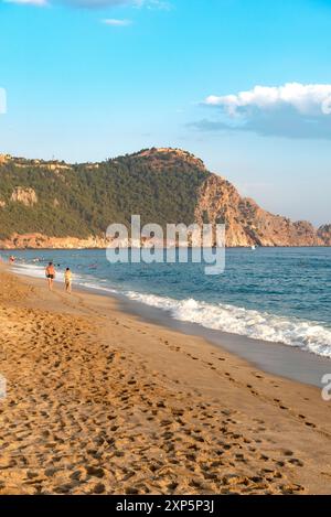 Una coppia cammina lungo una spiaggia vuota di Cleopatra al tramonto nella località turistica turca di Alanya, sulla costa mediterranea della Turchia, la riviera turca. Foto Stock