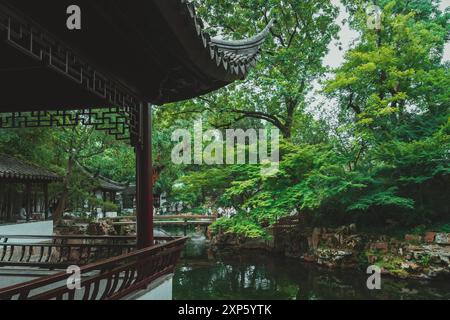 Suzhou, Cina - 11 giugno 2024: Un padiglione in legno che si affaccia su uno stagno e un ponte nell'umile Administrator's Garden di Suzhou, Cina. Foto Stock