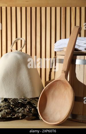 Frusta per sauna in quercia, cappello in lana di feltro, asciugamani, secchio e mestolo su una superficie in legno Foto Stock