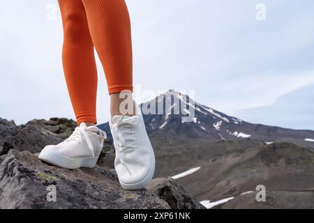 Primi piani gambe irriconoscibili appartenenti alla modella fitness femminile. Fit donna che indossa leggings skintight arancioni da palestra, sneaker durante le escursioni e i trail runni Foto Stock