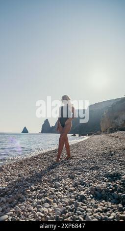 Costume da bagno donna in nero che cammina su una spiaggia di ghiaia Foto Stock