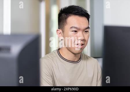 Uno studente universitario maschile è attualmente seduto davanti ai monitor del computer, coinvolgendo lo schermo in modo coinvolgente Foto Stock