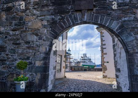 Un sentiero in pietra conduce attraverso una grande porta ad arco verso la storica fortezza di Bergenhus. La torre in stile medievale e le mura in pietra creano un senso di Foto Stock