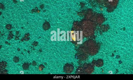 Pedana Top Down con acqua cristallina color smeraldo. Kayak giallo paddleboard, vela con barriera corallina e mare tropicale. Persone che praticano sport, relax, svago, vacanze estive. Vista aerea con il drone ridotto Foto Stock