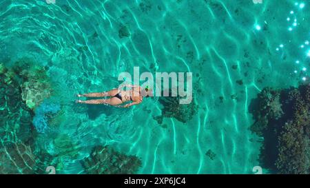 Vista aerea di una donna che fa snorkeling nelle acque turchesi, esplorando una barriera corallina. L'immagine evoca un senso di avventura e libertà, invitando gli spettatori a sperimentare la bellezza del mondo sottomarino Foto Stock