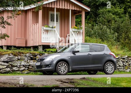 KINSARVIK, NORVEGIA - 13 AGOSTO 2016: Auto Suzuki Swift grigia nel paesaggio norvegese e case Foto Stock