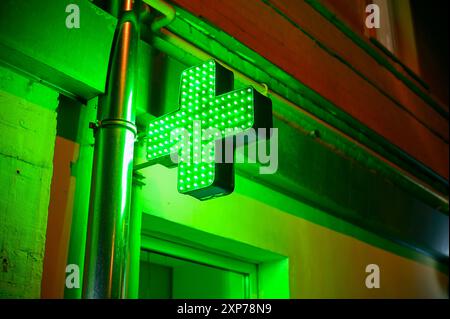 Croce verde luminosa di notte come segno della farmacia Foto Stock