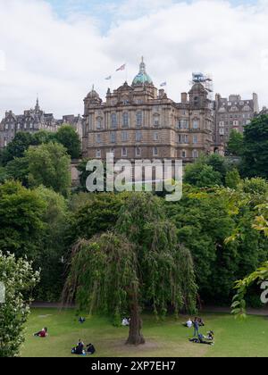 Persone che si rilassano nei lussureggianti giardini di Princes Street in una giornata estiva con Bank of Scotland sul tumulo alle spalle. Edimburgo, Scozia, 3 agosto 2024 Foto Stock