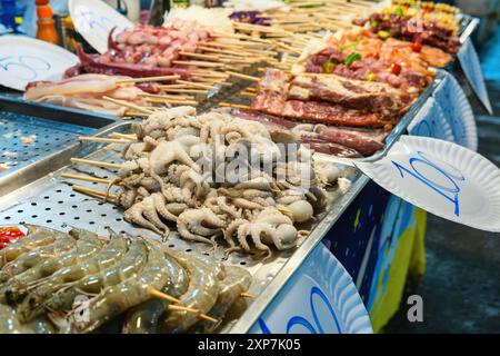 Assortimento di piatti a base di pesce e spiedini di carne. Polpi crudi, gamberetti e carne su bastoncini di legno. Cibo tailandese al mercato notturno. Cibo asiatico in Foto Stock