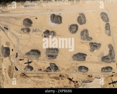 Estrazione di sabbia. Macchine e camion che lavorano su miniere di sabbia. Miniera di sabbia per scavi a cielo aperto. Vista aerea di una miniera di sabbia nella foresta con drone. Foto Stock