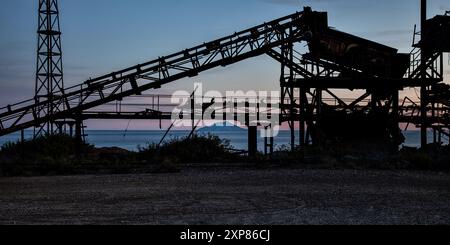 Macchinario arrugginito della miniera di ferro abbandonata del Vallone a Capoliveri all'Isola d'Elba, con il mare e l'isola di Montecristo sullo sfondo Foto Stock