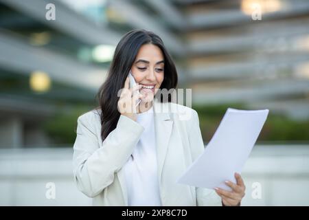 Donna d'affari che parla al telefono e che esamina documenti all'aperto Foto Stock