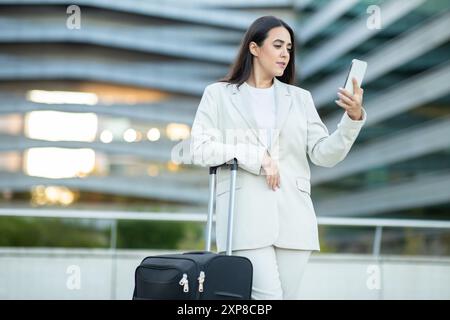 Donna in tuta bianca che utilizza il telefono, porta bagagli in città Foto Stock
