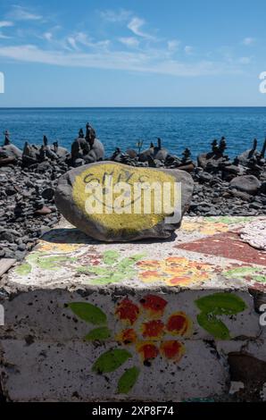 Grande ciottolo dipinto di giallo su una recinzione dipinta di una spiaggia. Torri di pietra nel backgroun e nell'acqua blu dell'oceano Atlantico. Cielo blu con clou bianco chiaro Foto Stock