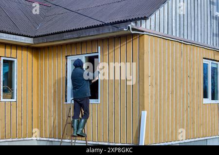 Rifinitura del telaio e del pannello della casa rurale sul lato della facciata, il conciatetto installa gli stipiti metallici sull'apertura della finestra. Foto Stock