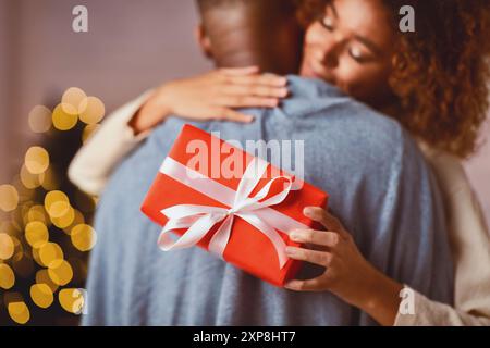 Amorevole donna afro abbracciando il marito, tenendo regalo di natale Foto Stock