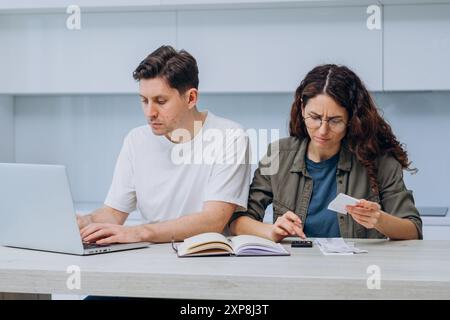 Un paio di persone che lavorano insieme sulle finanze a casa, con un notebook, un notebook e una calcolatrice, incentrati sul budget e sulle spese. Le donne contano e annotano le spese in un notebook. Foto Stock