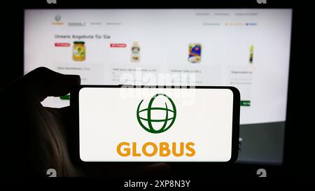 Persona che detiene un cellulare con il logo della società di vendita al dettaglio tedesca Globus Holding GmbH Co. KG davanti alla pagina Web aziendale. Mettere a fuoco il display del telefono. Foto Stock