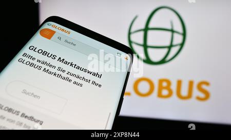 Telefono cellulare con sito web della società di vendita al dettaglio tedesca Globus Holding GmbH Co. KG davanti al logo aziendale. Mettere a fuoco in alto a sinistra sul display del telefono. Foto Stock