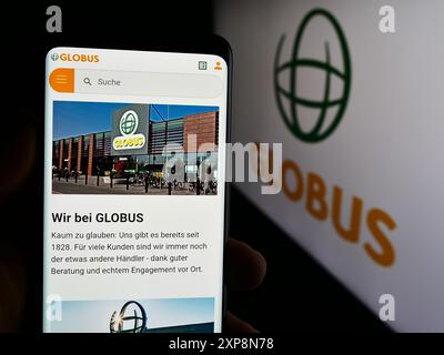 Persona che possiede uno smartphone con pagina web della società di vendita al dettaglio tedesca Globus Holding GmbH Co. KG davanti al logo. Messa a fuoco al centro del display del telefono. Foto Stock