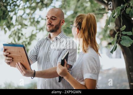 Due colleghi discutono di progetti all'aperto utilizzando tablet e notebook in un parco Foto Stock