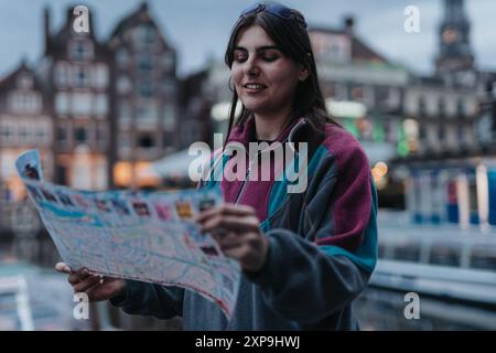 Giovane ragazza che esplora Amsterdam con una mappa della città, scoprendo nuovi luoghi e godendosi le visite turistiche Foto Stock