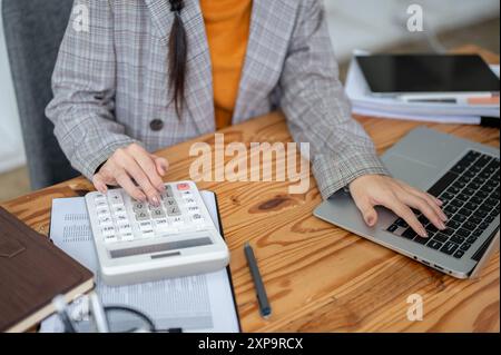 Immagine ravvicinata di una donna d'affari impegnata o di una contabile che lavora sul suo computer portatile e utilizza una calcolatrice, che lavora nel suo ufficio. Foto Stock