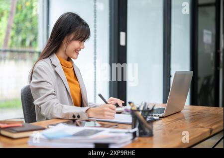 Una bella giovane donna d'affari asiatica o una donna contabile che usa una calcolatrice e lavora al suo incarico alla sua scrivania in ufficio. Foto Stock