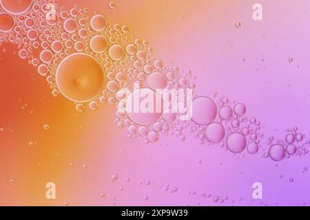 Macrofotografia di una miscela di olio e acqua che crea bolle su sfondo rosa e giallo. Foto Stock