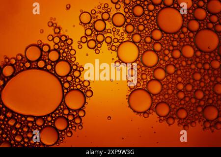 Macrofotografia di una miscela di olio e acqua che crea bolle su sfondo arancione e giallo. Foto Stock