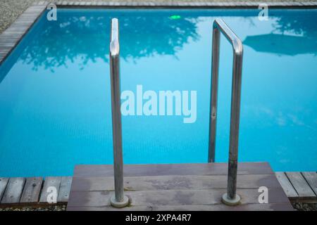 Scala in metallo che conduce ad una piscina blu chiaro con pavimento in legno e ghiaia. Primo piano per il design Foto Stock