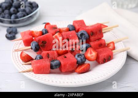 Spiedini con gustosi anguria, fragole e mirtilli su tavola bianca, primo piano Foto Stock