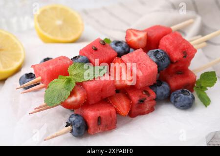 Spiedini con gustosi anguria, fragole, mirtilli e menta sul tavolo, primo piano Foto Stock